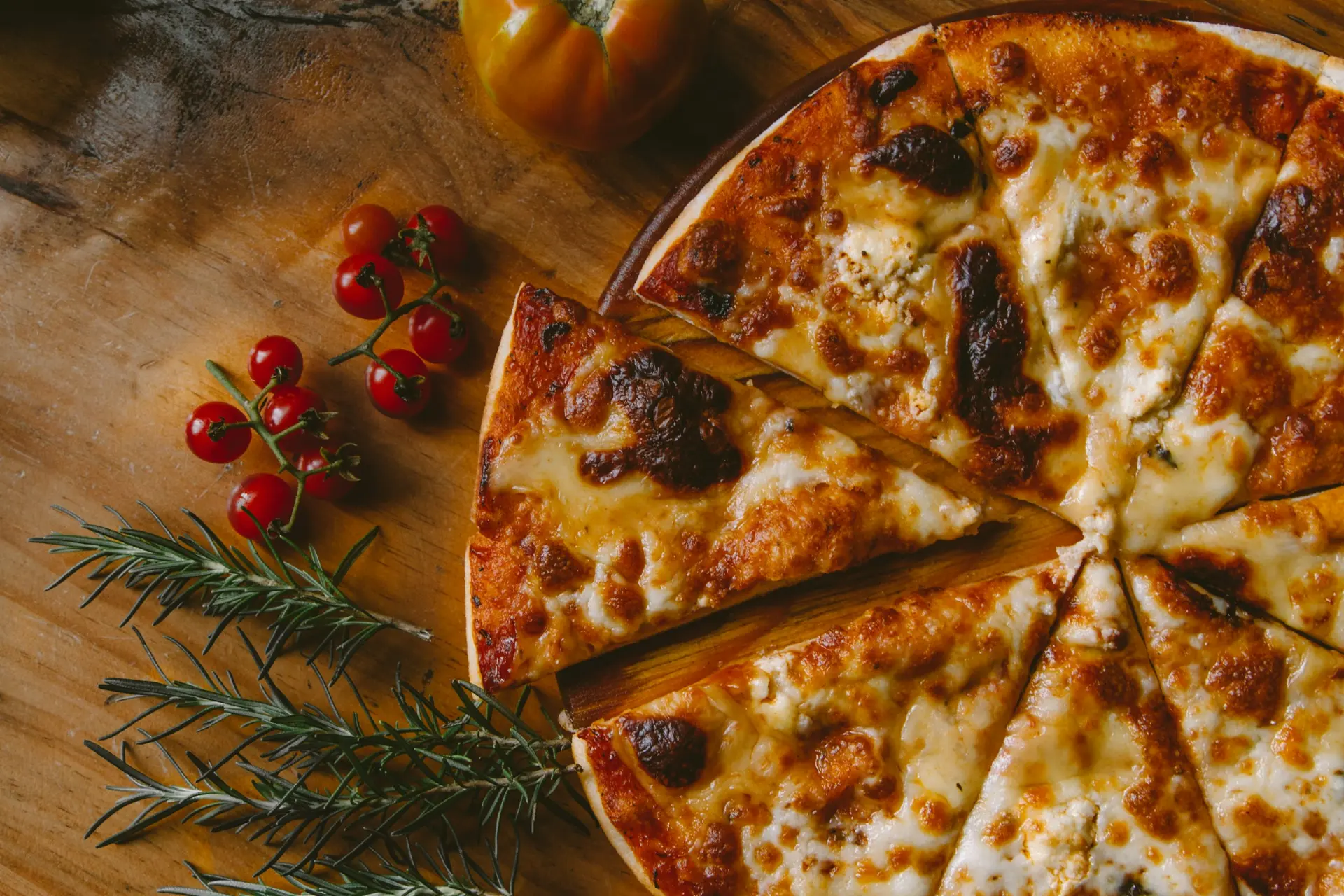 Wood-fired Neapolitan pizza sliced on a wooden board with cherry tomatoes and rosemary
